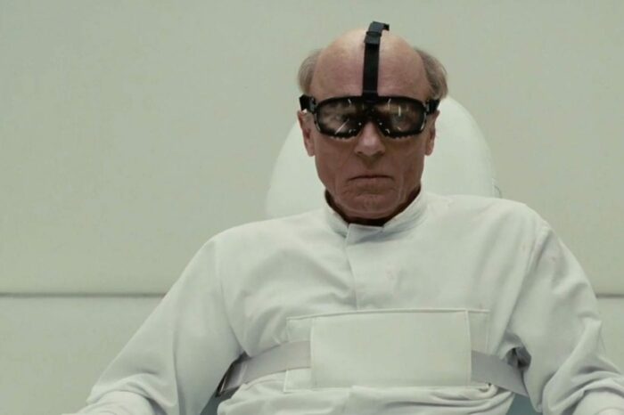 William is strapped to a chair in a psychiatric institution, wearing goggles