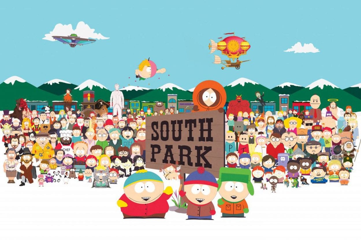 the four main south park characters out in the snow, next to the south park sign with many other charecters behind them