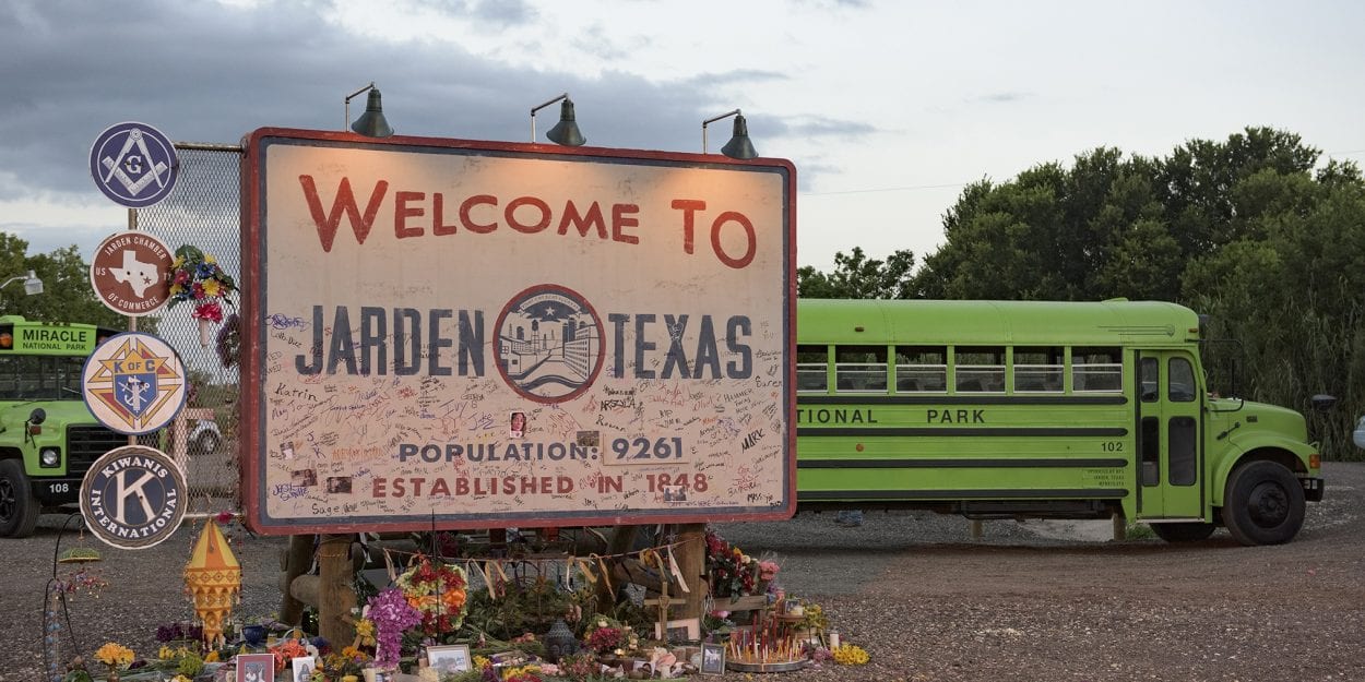 A welcome to Jarden, Texas sign with a school bus passing behind it