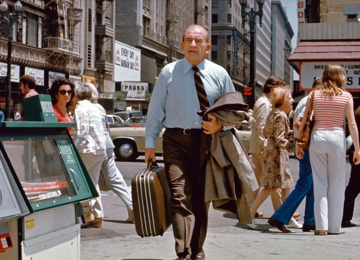 Lou walks down the street with a suitcase