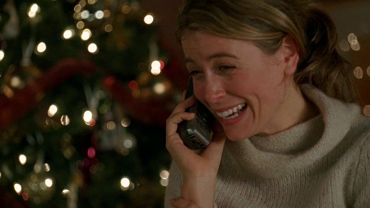 Penny holds a phone to her ear while standing in front of a Christmas tree