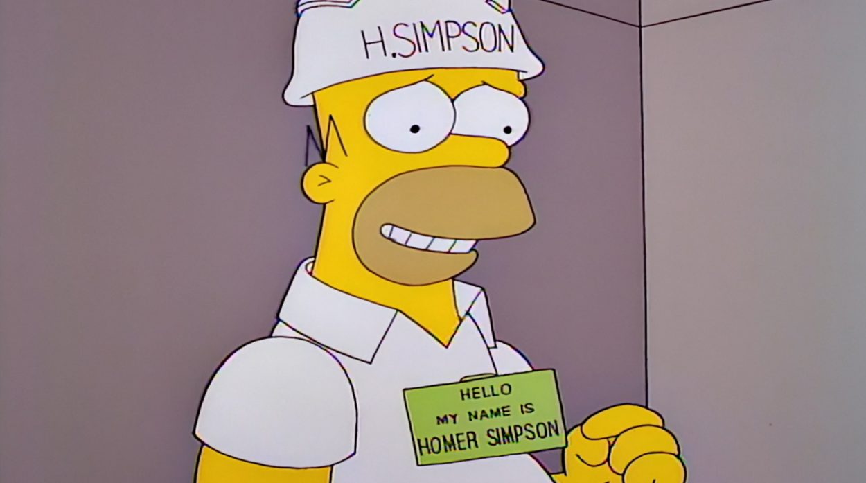 Homer wearing a hardhat with H. Simpson on it and a nametag