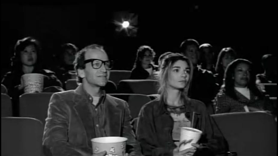 Maya sits in a movie theater with the fake Woody Allen, holding concessions