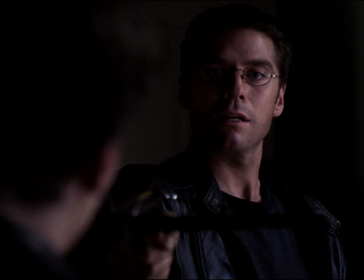 Wesley, wearing a leather jacket, points a crossbow at Angel