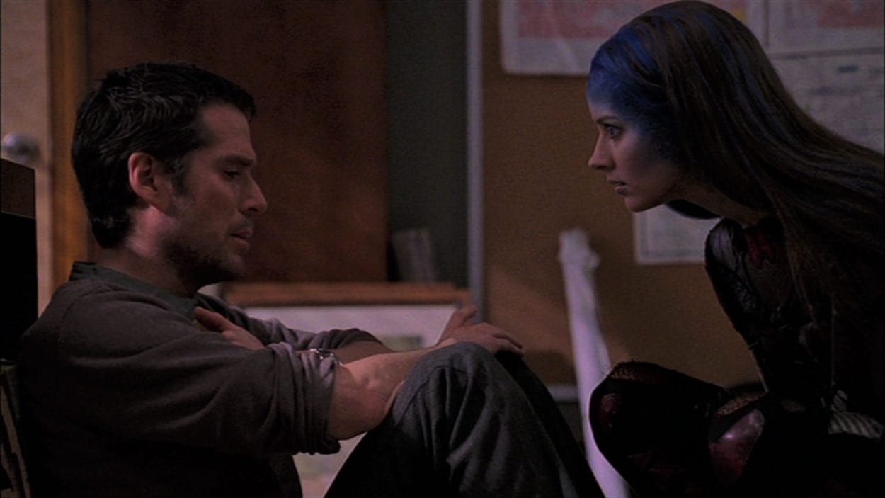 Wesley sits on the floor and Illyria crouches in front of him