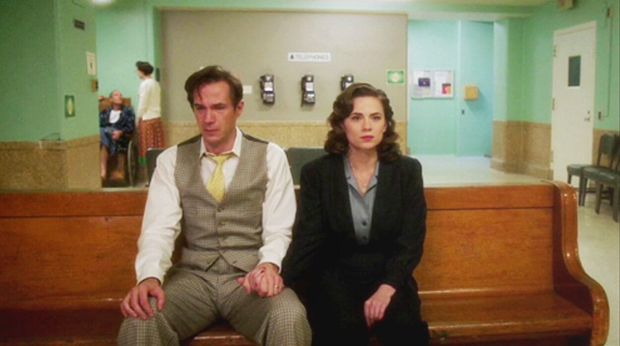 Edwin Jarvis (James D'Arcy) and Peggy Carter (Hayley Atwell) hold hands sitting in a hospital waiting room in "Agent Carter"