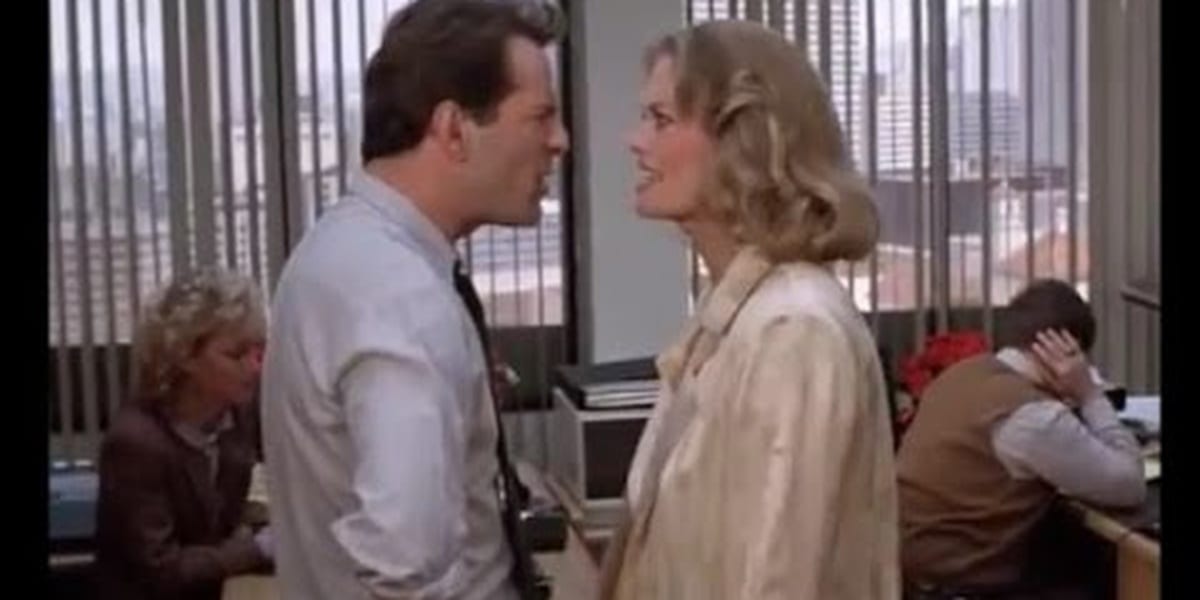 David and Maddie in one another's faces, their expressions contorted into anger as they argue, people in cubicles in the background, one man covering his ear in Moonlighting
