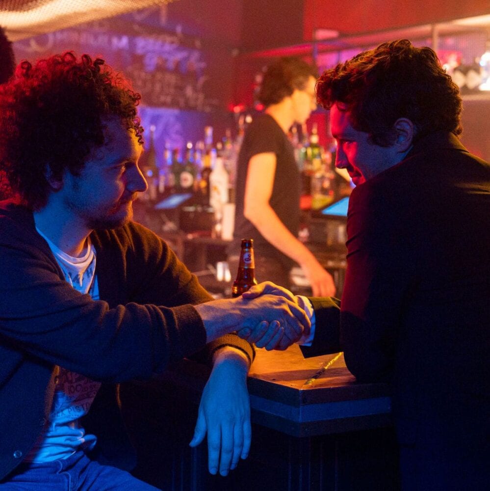 Simon and Ben shake hands in a bar.