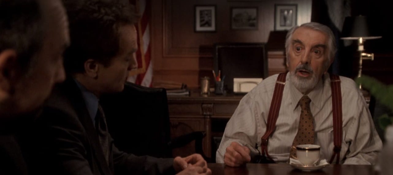 Toby and Josh sit at a table with a startled Chief Justice Ashland in the center of the frame. 