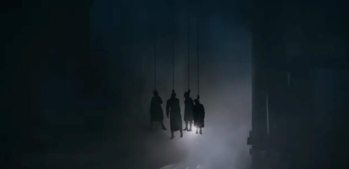 the silhouettes of 4 people hanging by their necks from the above bridge as a train is about to pass through