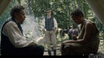 A shocked John Brown (Ethan Hawke) sitting inside a tent to the left and Henry "Little Onion" Shackleford (Joshua Caleb Johnson)making a terrible face after taking a bite from an onion sitting to the right while John Brown Jr. stands in the center between them with cups in his hands.