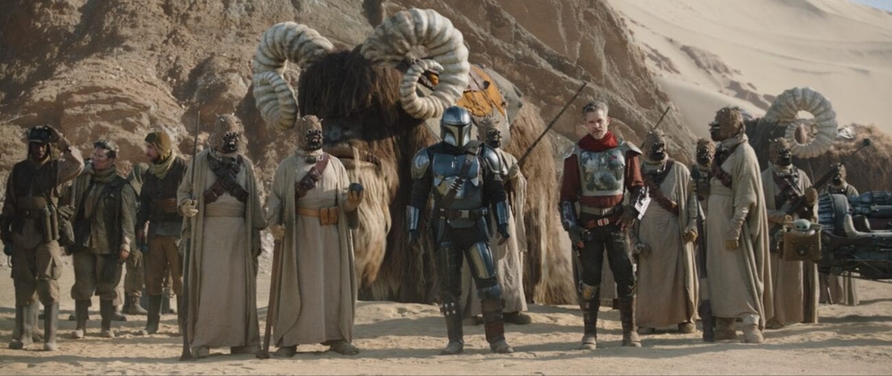 The Mandalorian, Cobb Vanth and Tusken Raiders stand in the desert, wit a Bantha in the background