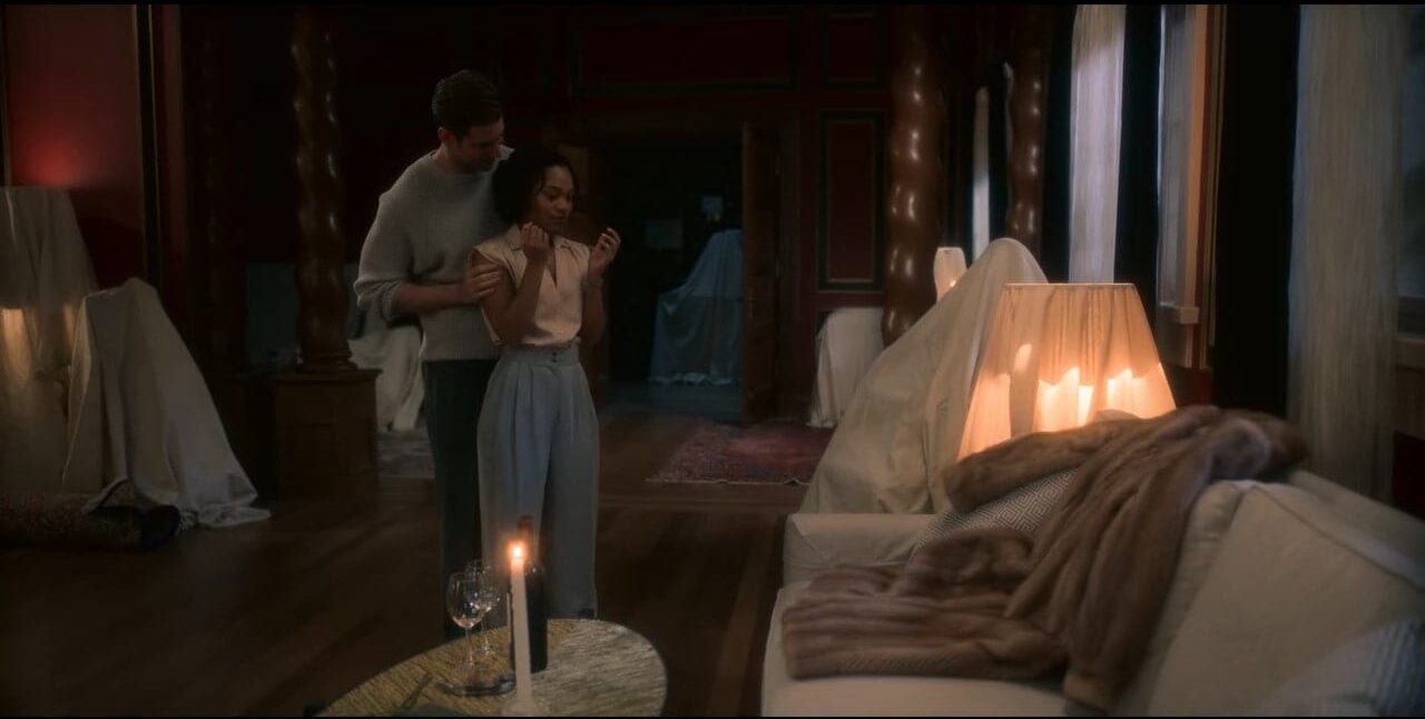 Peter holds Rebecca's arms as he presents her with a fur coat that lies on a couch