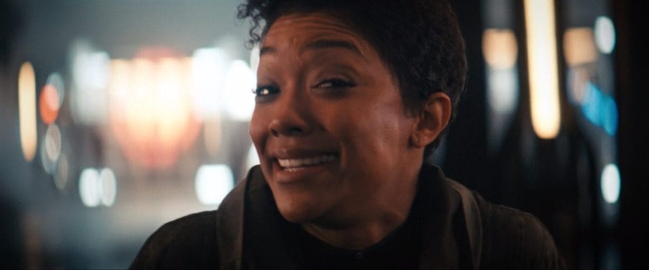 Michael Burnham (Sonequa Martin-Green) in the center of the shot looking toward the camera making a goofy face, the background is a series of blurry lights