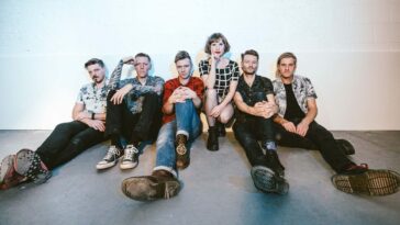 The six member of the band Skinny Lister sitting on the floor looking into the camera