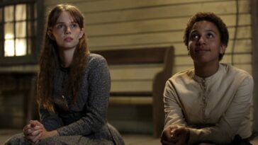 Annie Brown (Maya Hawke) and Onion (Joshua Caleb Johnson) sitting on the porch of a white house with a brown bench behind them, looking up at the sky