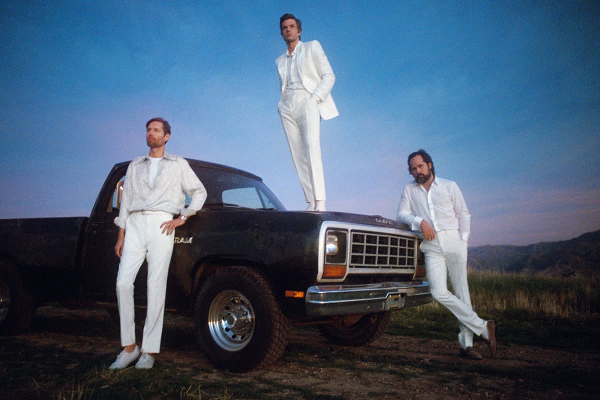 The three active members of the killers are dressed in white and leaning against a car