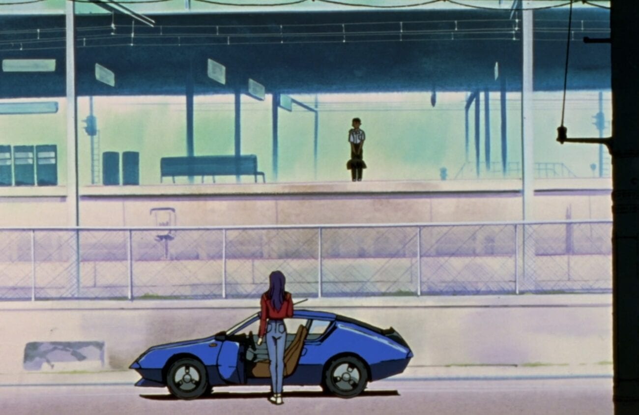 Shinji standing on the train platform in the background while Misato stands by her car in the foreground, looking at him