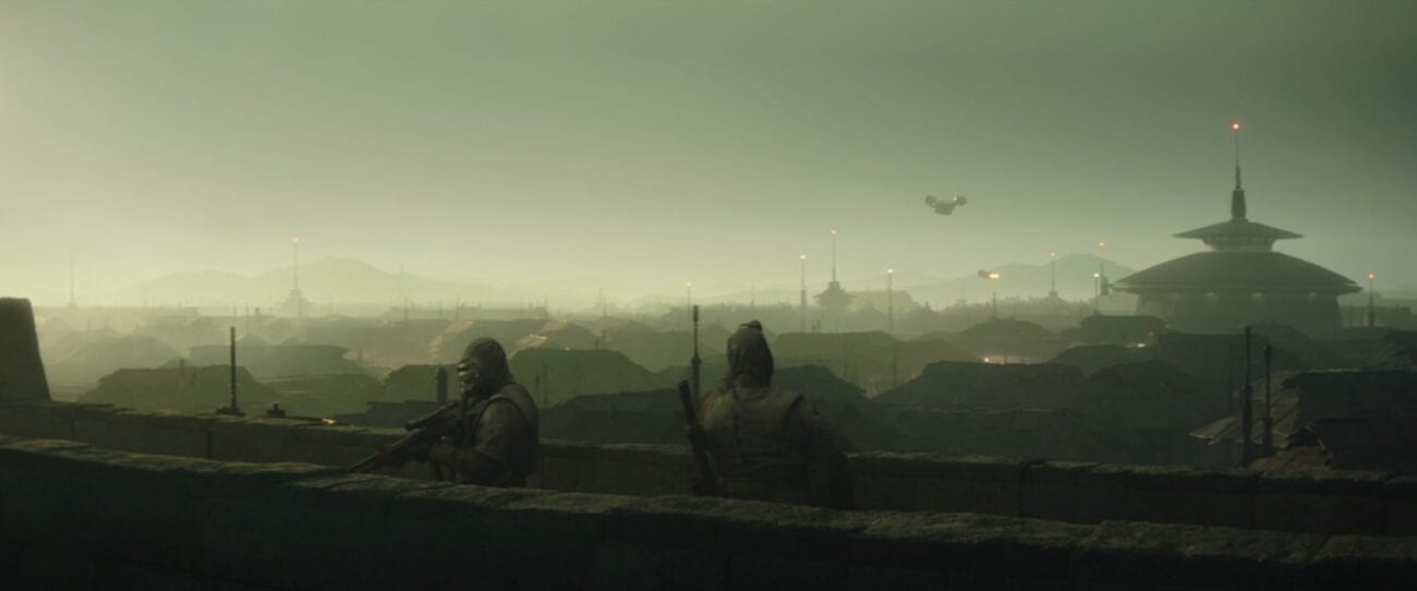 The Razor Crest flies over the town of Calodan, with two guards on the city wall