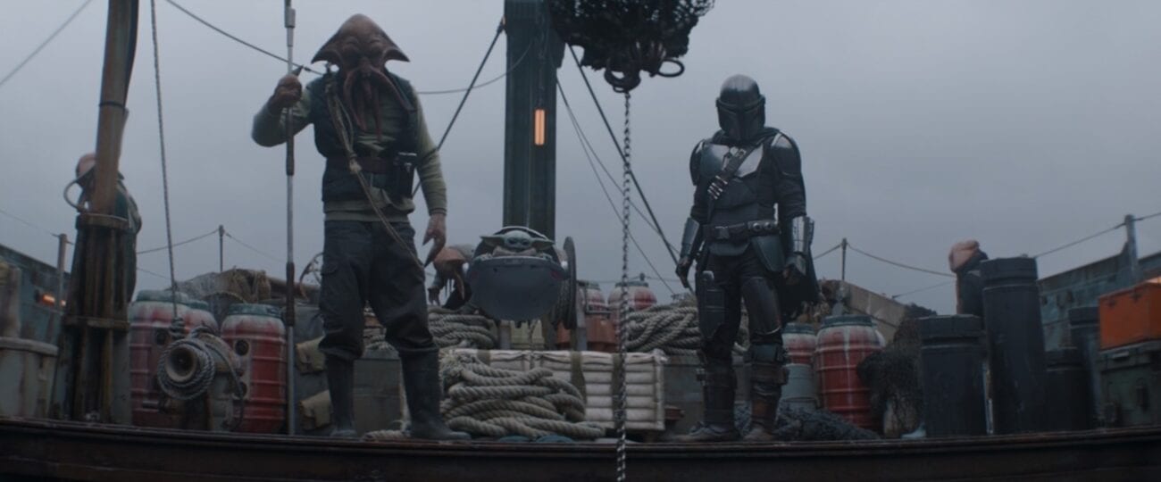 A Quarren alien, The Child (Baby Yoda), and The Mandalorian stand on the deck of a ship