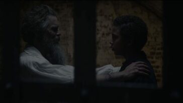 John Brown (Ethan Hawke) with his arms on Onion's (Joshua Caleb Johnson) shoulders in a darkened jail cell seen through the bars