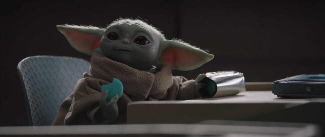 The Child (Baby Yoda) sits at a school desk eating a cookie he stole