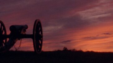 A canon in shadow on the left of the frame with a vivid red, orange, and purple sunset on the horizon