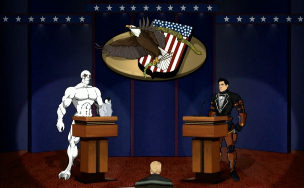 The mutant Killface and Xander Crews on a debate stage in front of podiums. Crews is wearing a tuxedo shirt and Killface has a penguin on his podium.