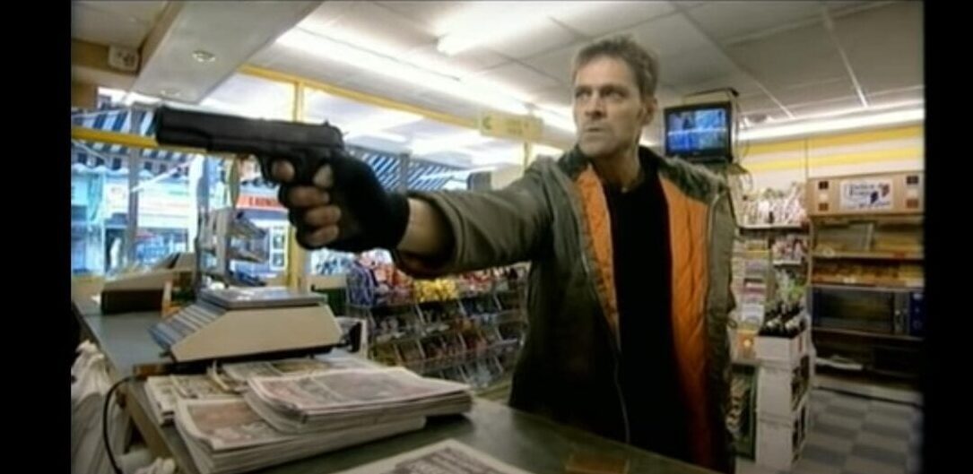 Mark Heap holds a man up in a shop with a gun, demanding his change in episode 2
