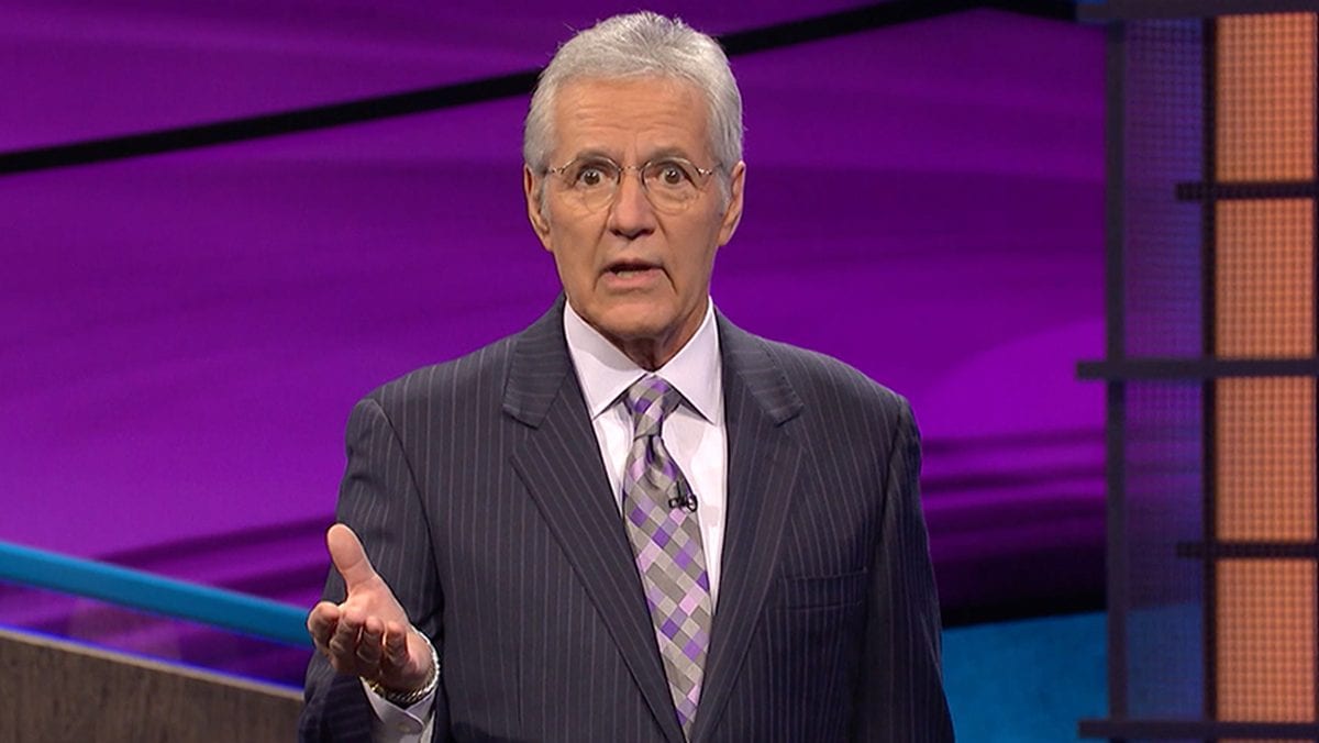 Alex Trebek with a hand facing upwards in front of him