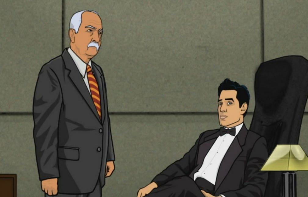 Xander Crews in a tux sitting at his desk, standing next to him is his business partner Stan.