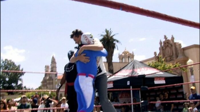 John hugs a luchador in the middle of a wrestling ring