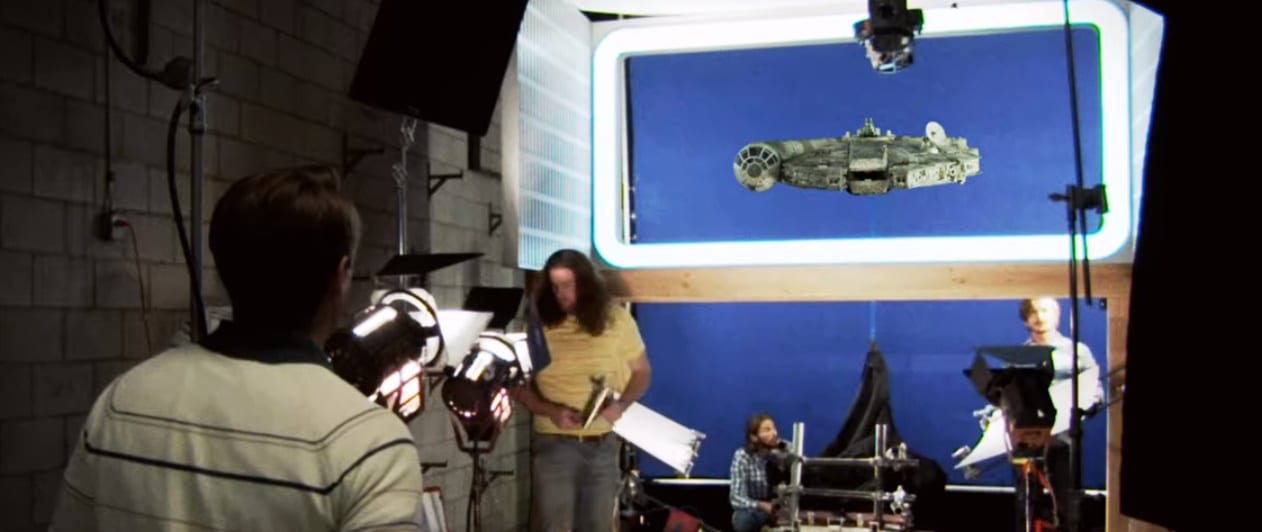 A young Jim Swearingen walks into a studio set where the crew of Star Wars is taking shots of the Millenium Falcon model, cameras and lights are on the model and several 70s figures are in the background