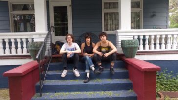 The three female members of Palberta sitting on the steps outside a house looking at the camera