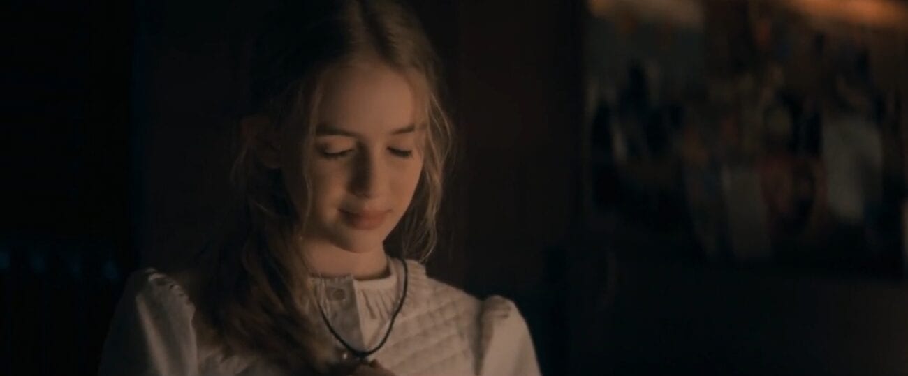 Young Nadine fingers her necklace, eyes closed and a slight smile on her face in The Stand Episode 3