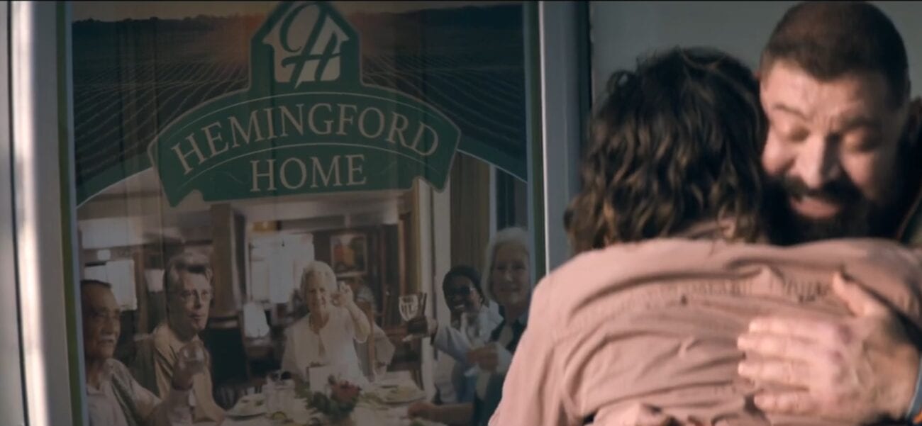Tom embraces Nick, a poster advertising Hemingford Home behind them in The Stand Episode 4