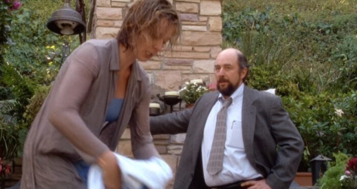 C.J. (Allison Janney) dries off with a towel while Toby (Richard Schiff) stands in front of brick wall and looks on