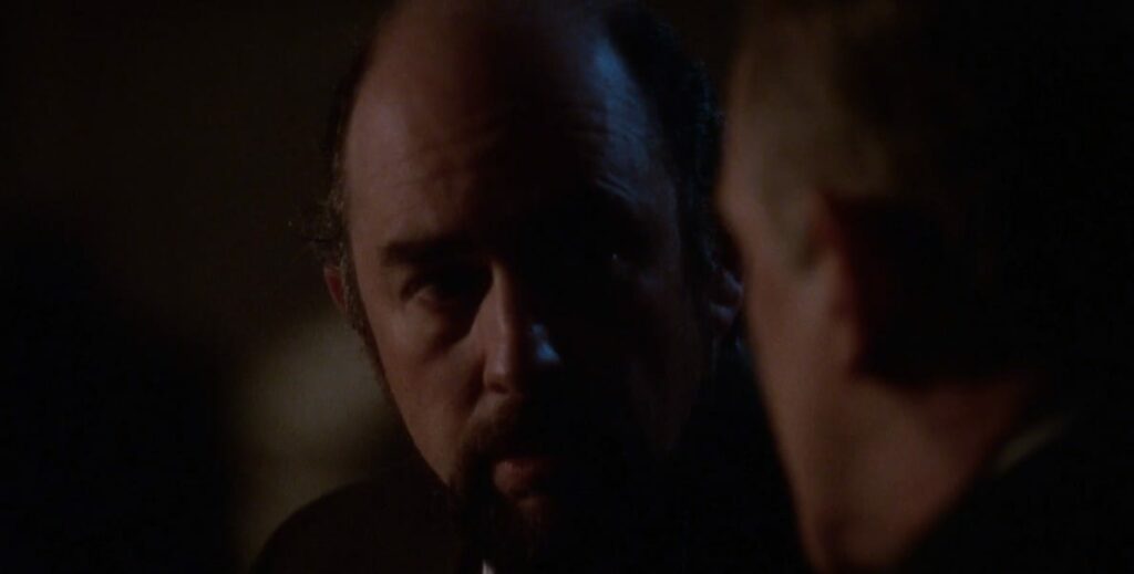Toby (Richard Schiff) in a dark portico looking at Leo (John Spenser) 