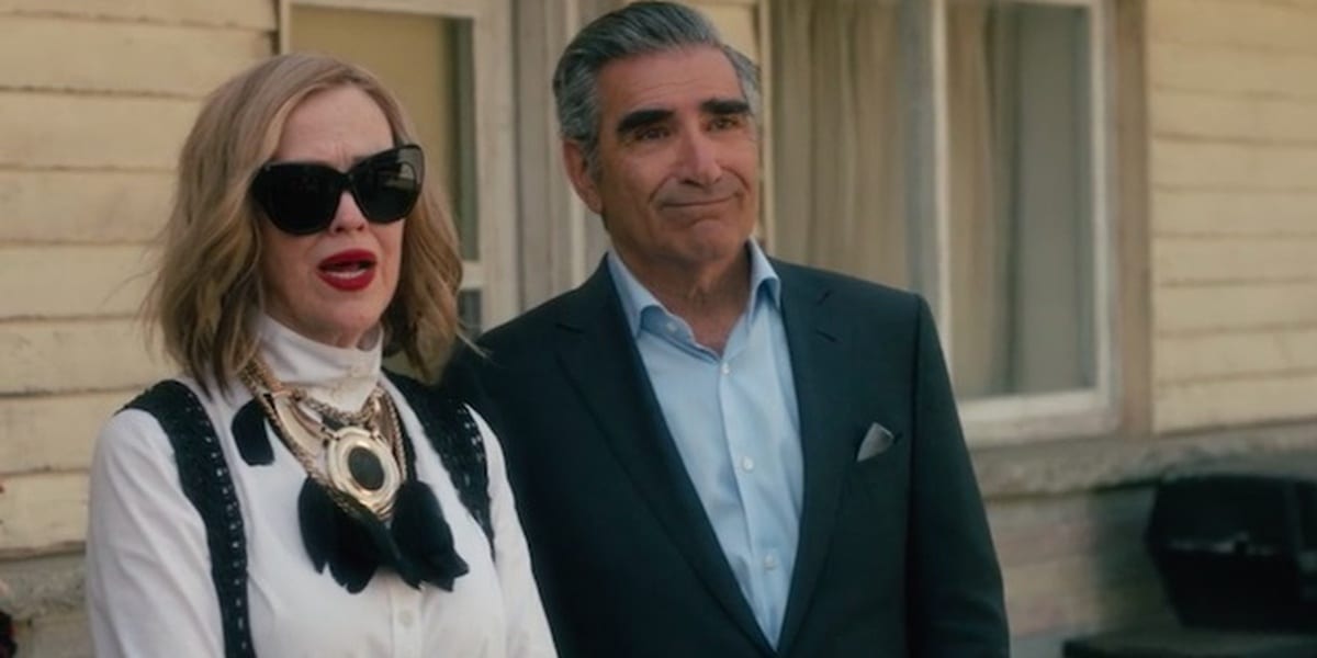Moira and Johnny standing outside the motel, Moira wearing sunglasses and Johnny a suit in Schitt's Creek