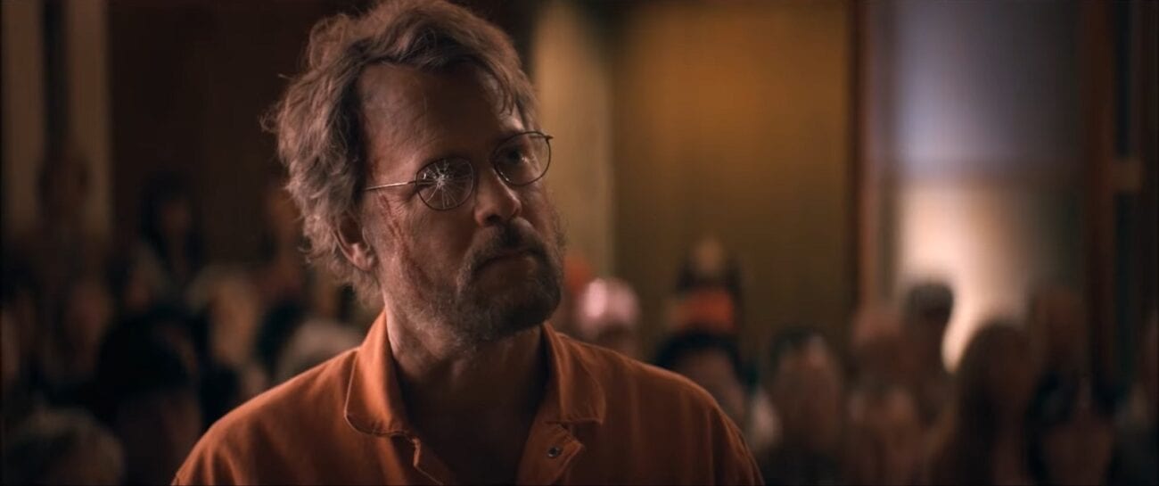 Glen stands in a courtroom, clothed in an orange prison jumpsuit, the right lens of his glasses broken in The Stand Episode 8