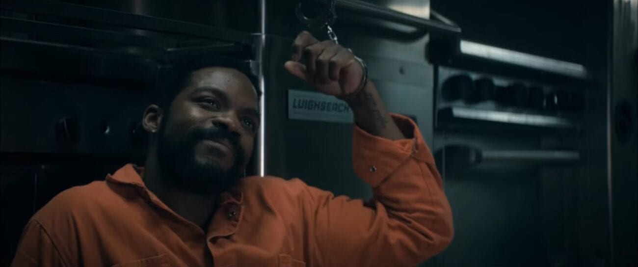 The Stand S1E8 - Larry sitting on the ground in an orange jumpsuit, handcuffed to a piece of kitchen equipement, smiling up at someone