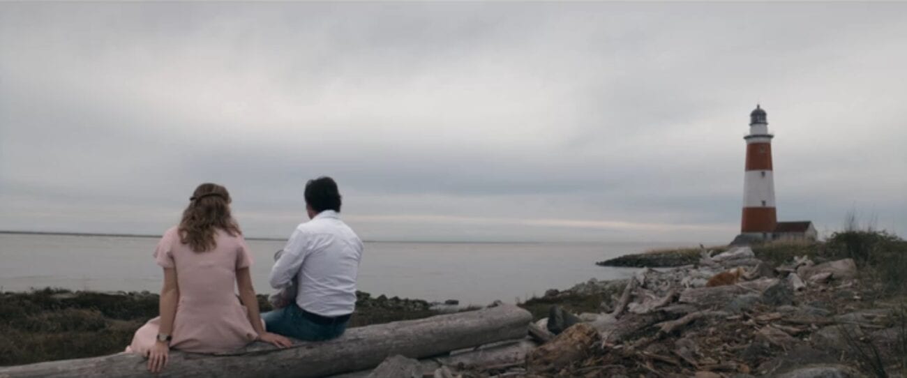 The Stand S1E9 - Frannie and Stu sit on a rocky Maine beach, looking out over the ocean, with a lighthouse nearby