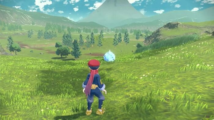 a pokemon trainer stands in a huge field, overlooking a rhydon