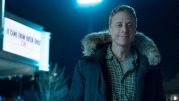 Alan Tudyk smirks with a sign reading "it came from outer space" behind him in Resident Alien