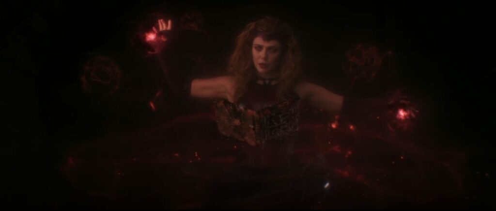 The Scarlet Witch holds a scary magic book in front of her while her arms are held up and spinning magic. Wanda's eyes glow red.
