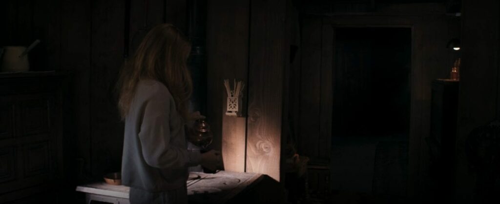 Wanda, back to camera, is pouring tea in an unlit room.