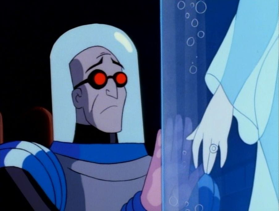 Mr Freeze, in his containment suit, looks longingly into the glass in front of him, where we see the arm of his frozen wife Nora.