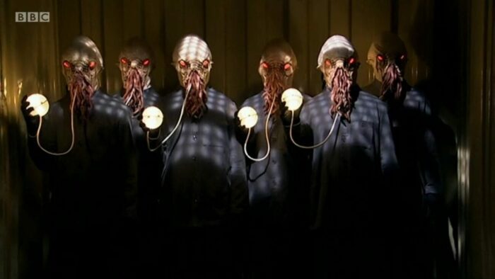 The Ood stand in a group, eyes glowing red, holding up their lit translation spheres