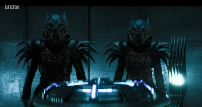 The two surviving Thijarians stand next to one another on their spaceship