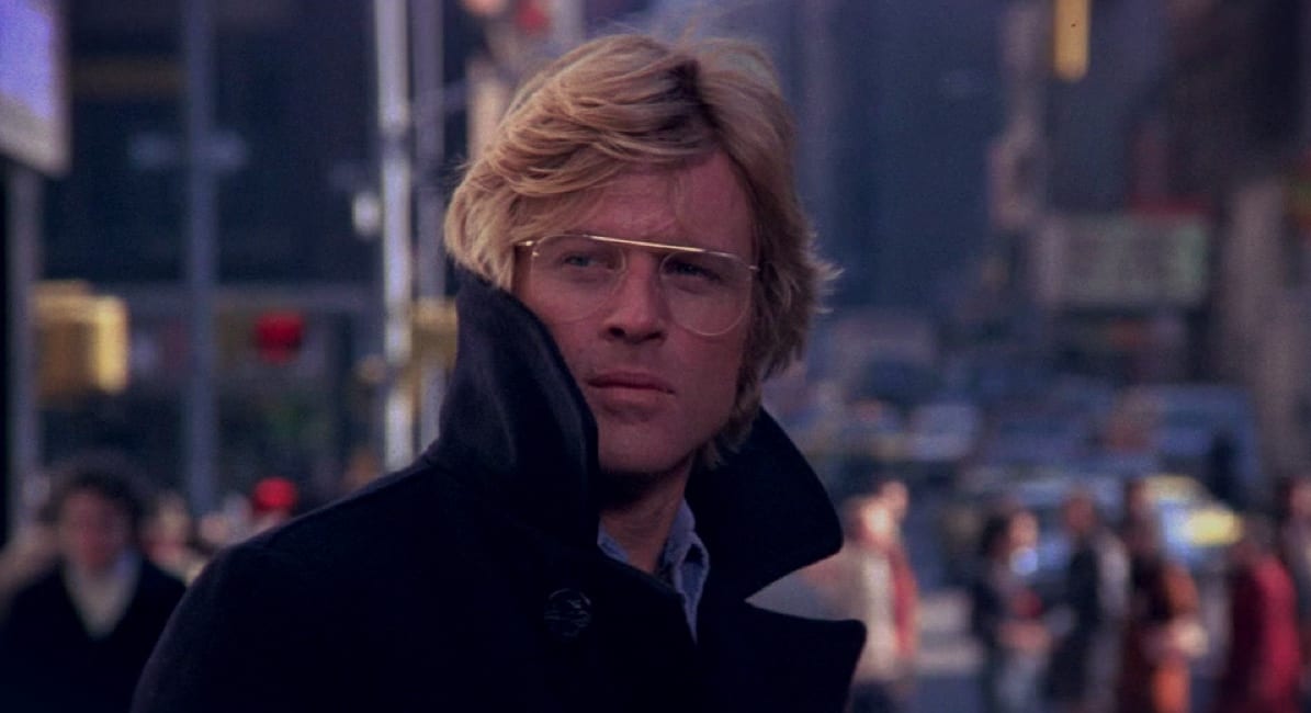 Robert Redford's Joe Turner is a quixotic survivalist, as he looks on wearing thin-framed glasses on a busy street that is out of focus behind him